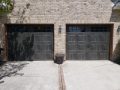 Matching black garage doors on a white brick home.