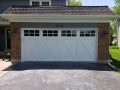 A white garage door with windows on a brick house.