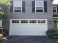 A white garage door with windows on a grey house.